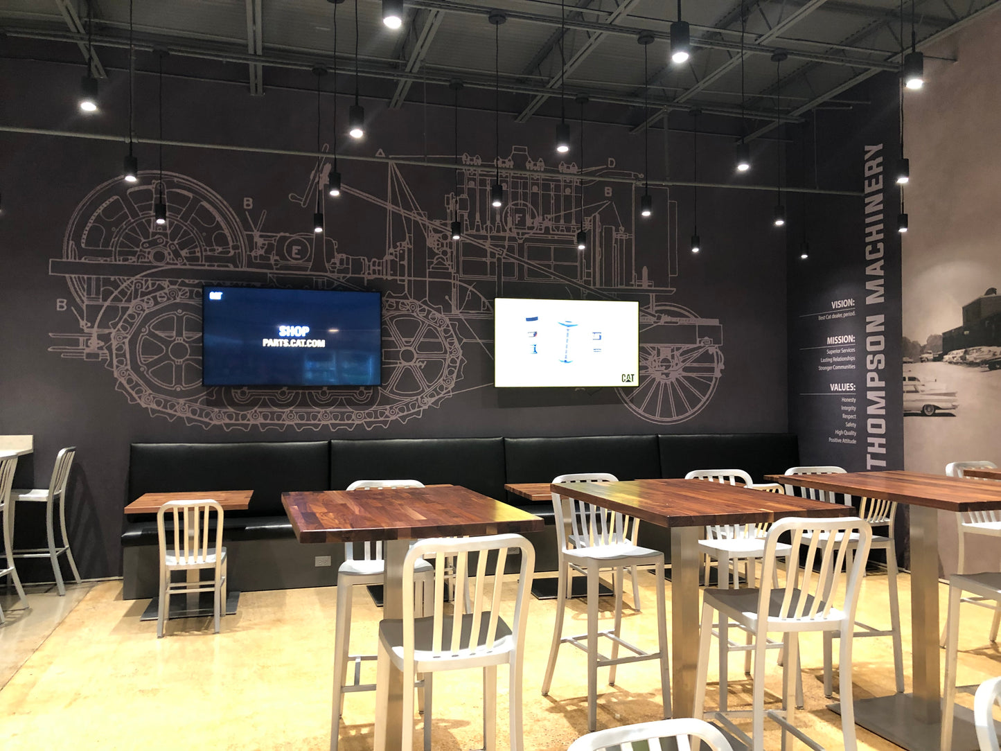 Modern cafe interior with tables, chairs, and digital displays on a black wall.