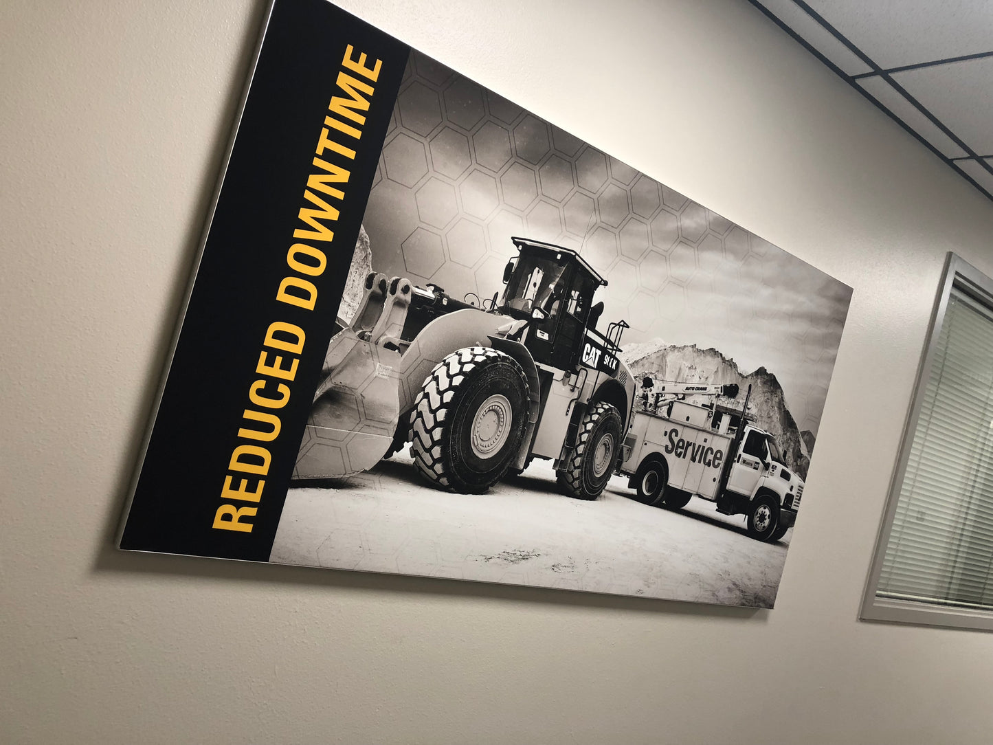 A wall-mounted silicone edge fabric panel featuring a black and white photograph of construction equipment with the text 'REDUCED DOWNTIME' printed on the image.